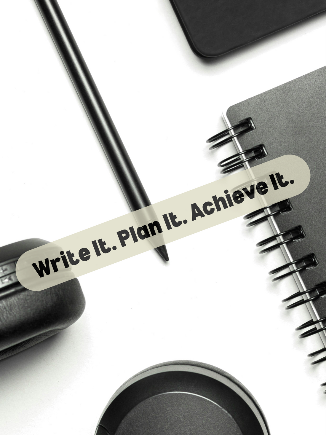 Motivational flat lay with spiral notebook, pen, and headphones featuring 'Write It. Plan It. Achieve It.' quote for goal setting and productivity