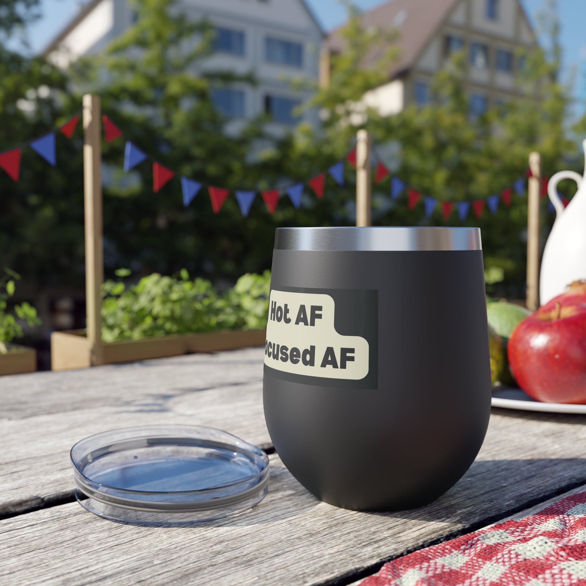 Black insulated wine tumbler with humorous label on a wooden table outdoors.